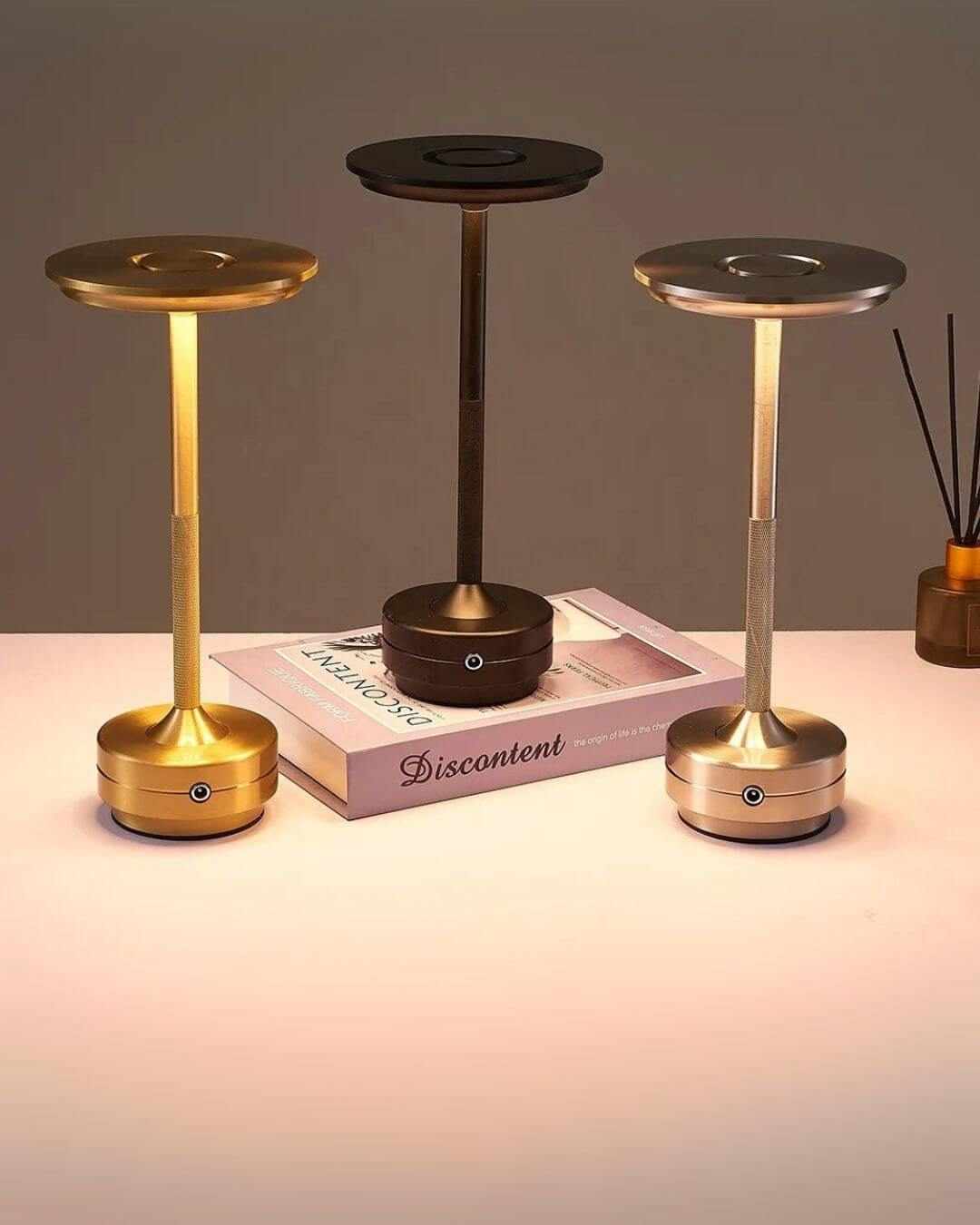 Three LumiHikari Base Lamps in gold, black, and silver finishes emitting warm ambient light on a tabletop.