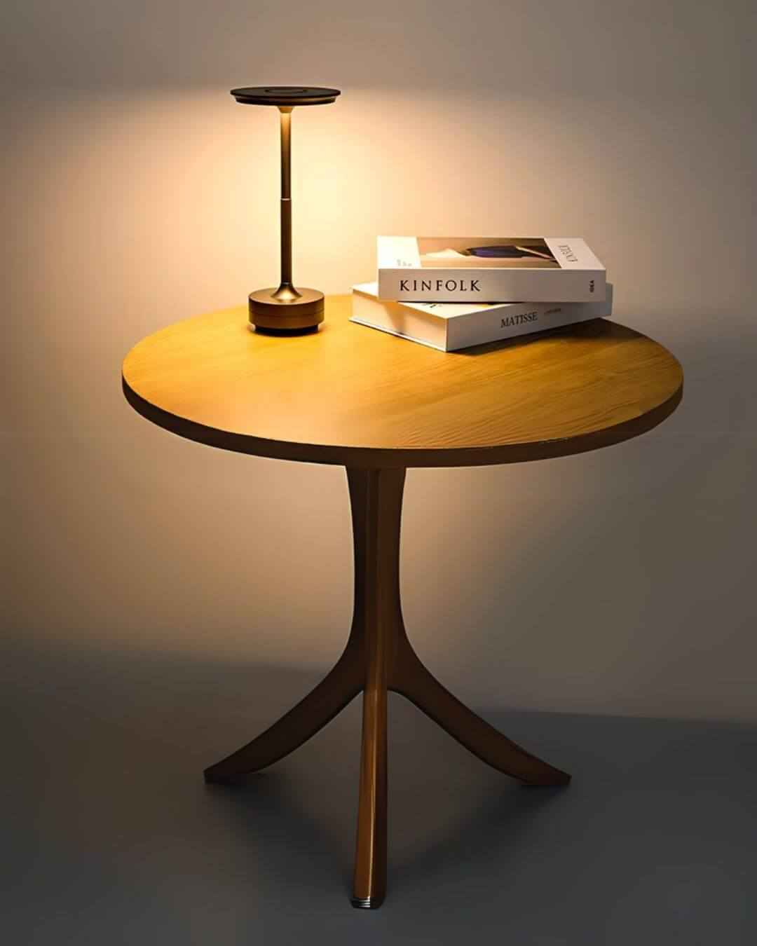 LumiHikari Base Lamp with sleek brushed metal finish on a round wooden side table emitting warm ambient light next to stacked books