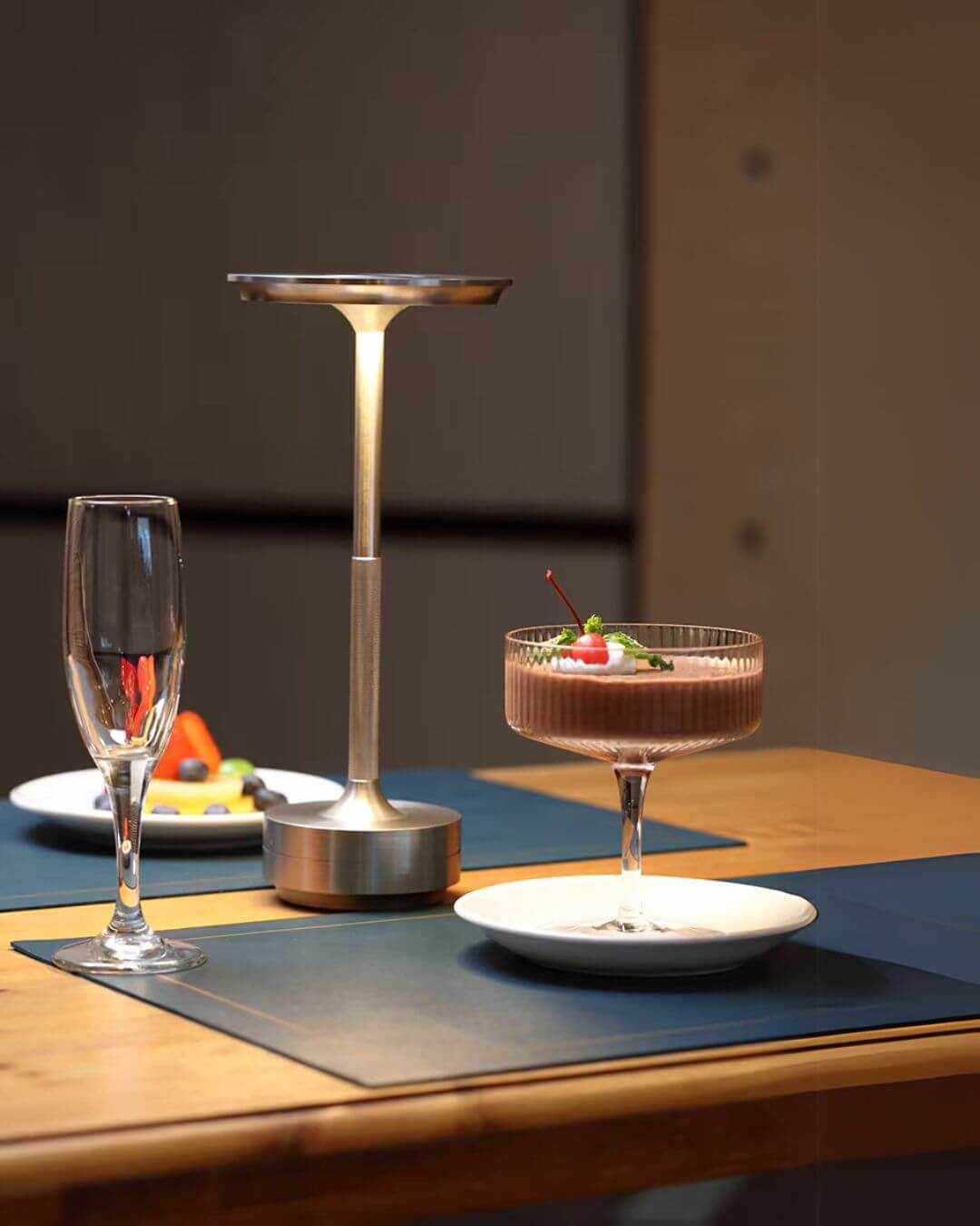 LumiHikari Base Lamp with brushed metal finish providing warm ambient light on a dining table next to a dessert and a wine glass