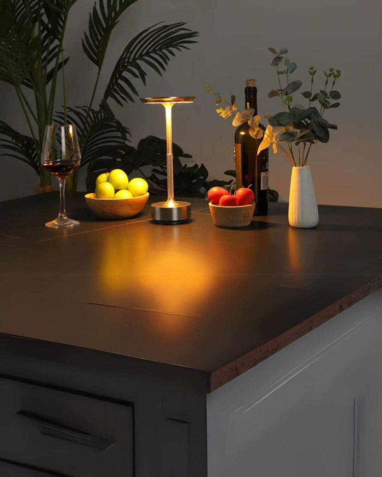 LumiHikari Base Lamp with warm ambient light on dark tabletop surrounded by fruit bowls and a vase